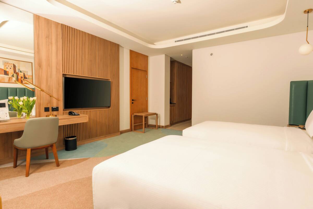A modern hotel room with a bed, desk, chair, television, and a small table.