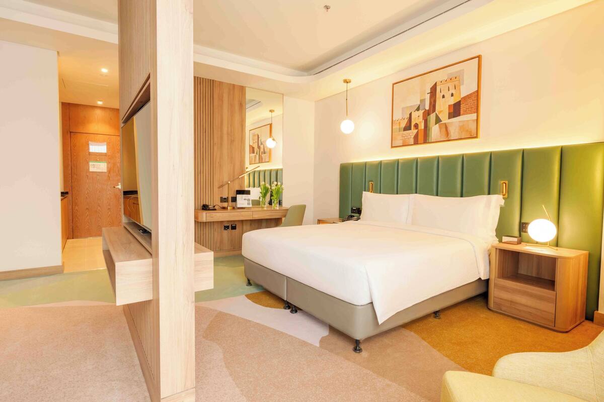 A hotel room with a bed, bedside table, nightstand, desk, chair, and a mirror.