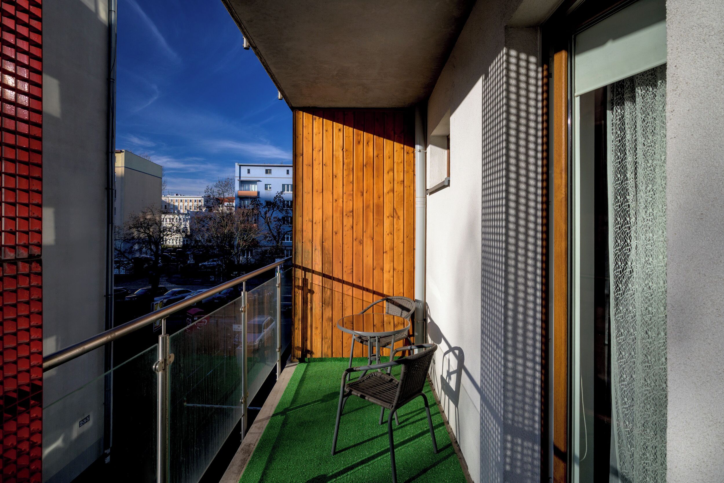 A balcony with a green artificial turf, a metal chair, and a wooden wall.