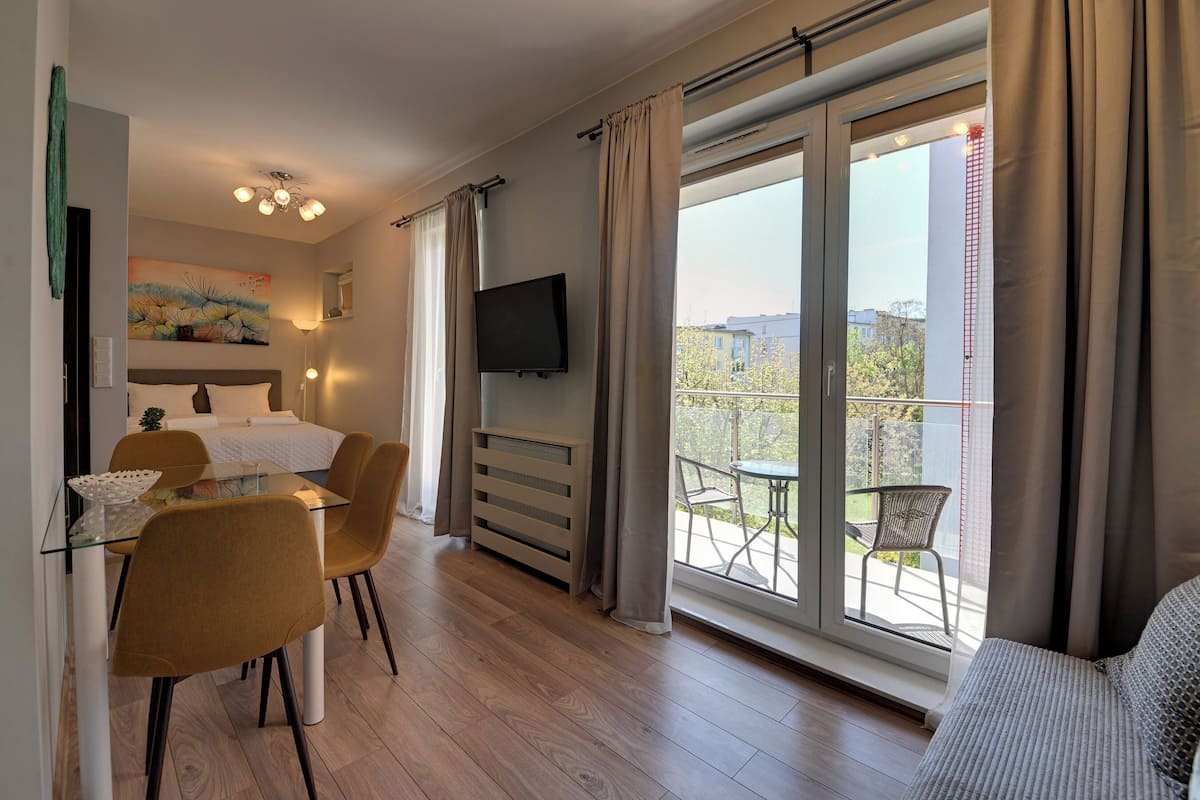 Una habitación moderna con cama, una mesa de comedor con sillas, televisor y balcón con mobiliario exterior.