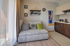 A living room with a sofa, a kitchen area, and a window with curtains. - RentPlanet - Studio Kościuszki (Wrocław)