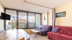 Ein Wohnzimmer mit einer Couch, einem Tisch, einem Fernseher und einem großen Fenster.