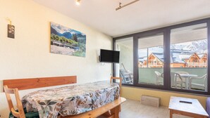 Ein Zimmer mit Bett, Fernseher, Fenster und Blick auf Holzhütten sowie einem Tisch.