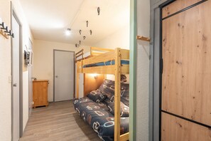 Un lit superposé avec un matelas à motifs, une armoire en bois et une porte dans une pièce dont le sol est recouvert de planches de bois.