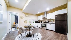 A compact kitchen with a dining area, featuring a round table, chairs, and modern appliances. - Sanctuary Suite - KingBed - Wifi - Near WEM/Rogers (Edmonton)