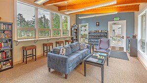 A cozy reading area with a blue sofa, bookshelves, and a large window offering a view of trees. - Aqua Vista Condo at Blue Heron Resort (Union)