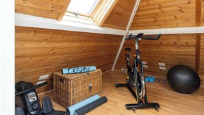 Academia com paredes de madeira, ventilador de teto, equipamentos de exercícios e uma bola de ginástica grande.