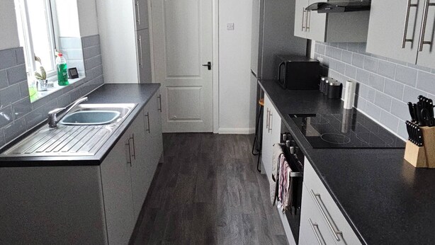 A modern kitchen with grey cabinets, a black countertop, a stainless steel sink, and a built-in oven. - Charming 3-bedroom Home in Doncaster, Perfect for Family, Friends & Contractors (Doncaster)