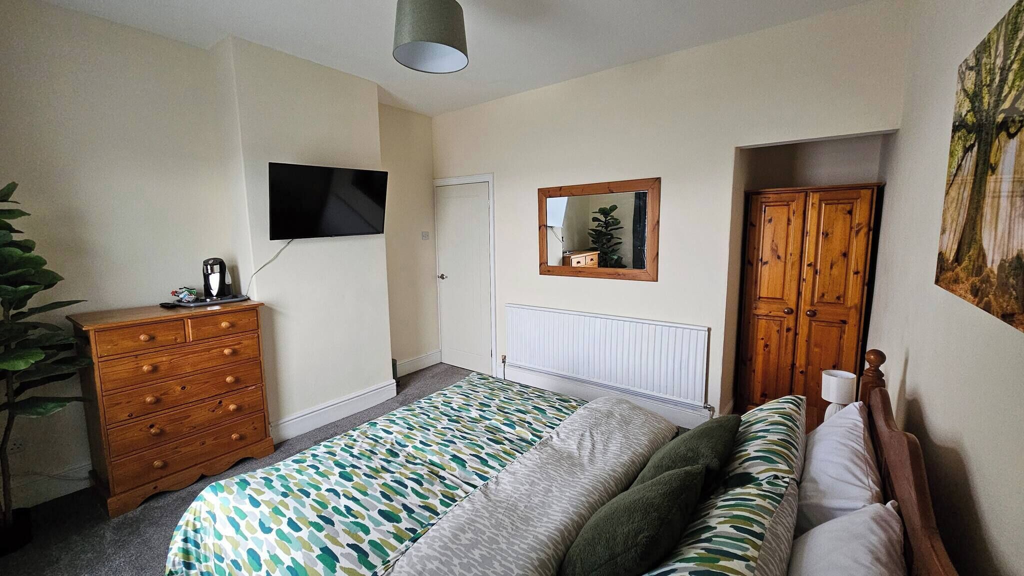 Un dormitorio con cama, cómoda, televisor, radiador, puerta y espejo.