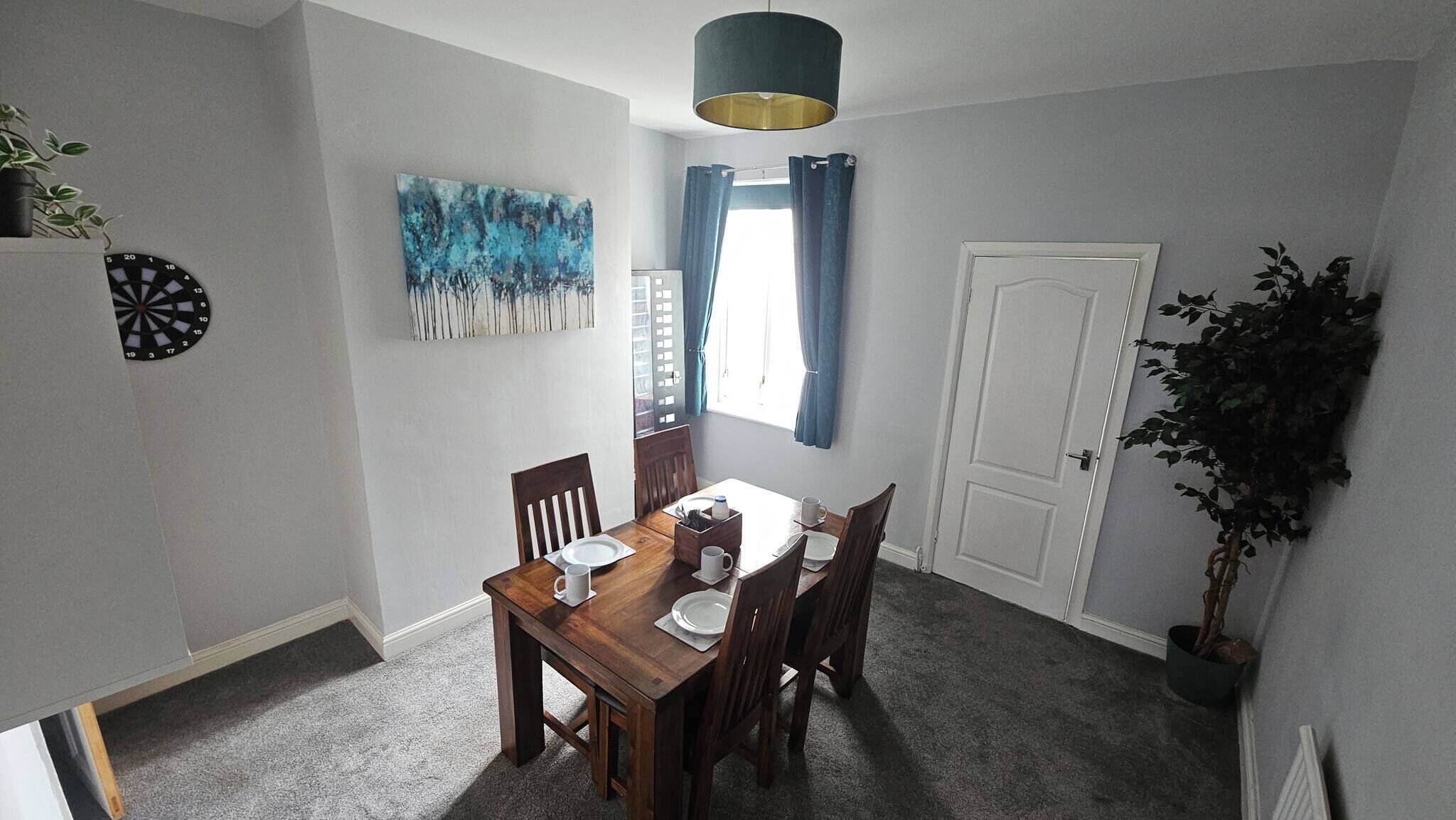 A dining area with a wooden table, chairs, a dartboard, and a painting on the wall.