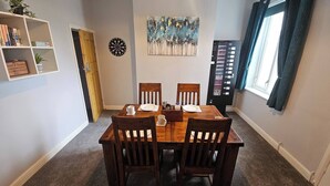 A dining area with a wooden table, four chairs, a dartboard, and a bookshelf with books. - Charming 3-bedroom Home in Doncaster, Perfect for Family, Friends & Contractors (Doncaster)