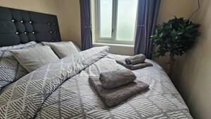 A neatly made bed with patterned bedding, a tufted headboard, and a potted plant beside the window. - Charming 3-bedroom Home in Doncaster, Perfect for Family, Friends & Contractors (Doncaster)