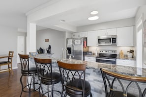 A modern kitchen with a central island, bar stools, stainless steel appliances, and white cabinetry. - Grand Ridge Retreat w Decks, TVs & Pool Access! (Osage Beach)