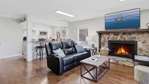 A living room with a fireplace, a black leather sofa, a coffee table, and a TV mounted above the fireplace. - Grand Ridge Retreat w Decks, TVs & Pool Access! (Osage Beach)