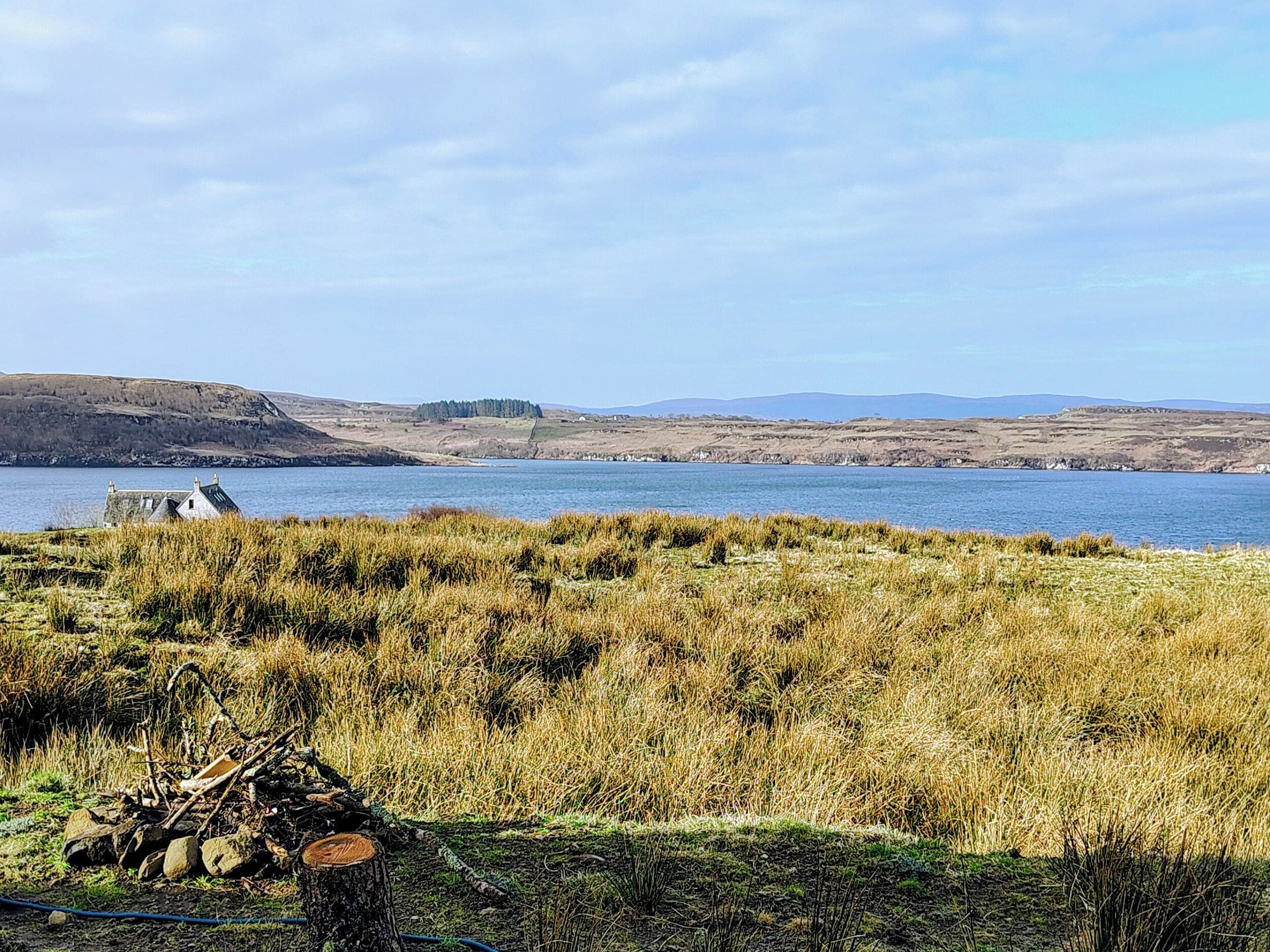 A coastal landscape with a body of water, grassy fields, and distant hills.