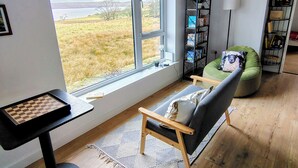 Ett rum med ett stort fönster, en bokhylla, en grön stol och ett schackbräde.