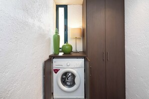 Ein kleiner Waschbereich mit einer Waschmaschine, einer grünen Flasche und einer Lampe auf einem Regal.