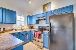 Eine Küche mit blauen Schränken, Edelstahlgeräten, einem Kühlschrank und einem Fenster.