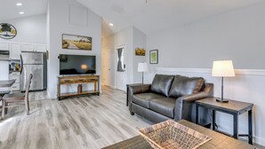 A modern living room with a leather sofa, a flat-screen TV, a dining area with a table and chairs, and a kitchen with cabinets and appliances. - Hot Tub Townhome Near Downtown Gatlinburg (Gatlinburg)