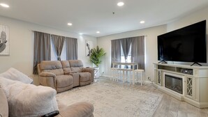 Ein modernes Wohnzimmer mit einem beigen Sofa, einem Relaxsessel, einem Flachbildfernseher und einem Kamin.