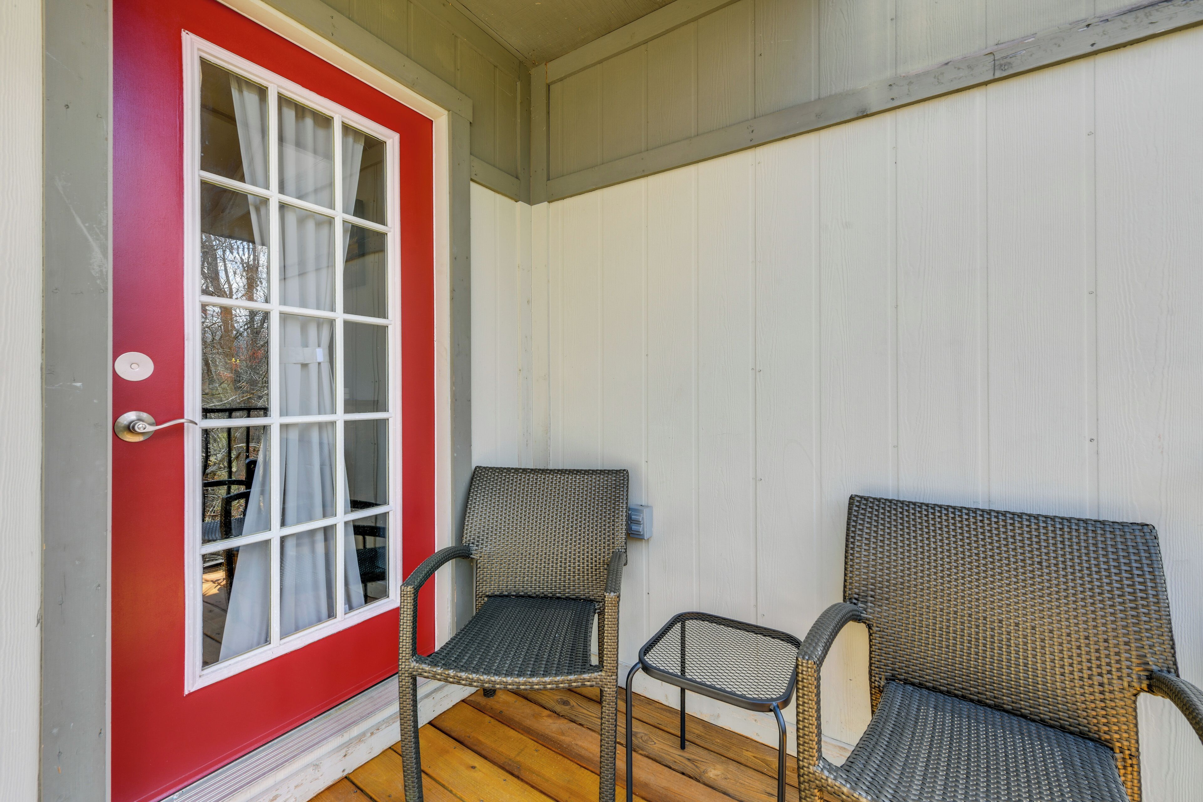 A porch with two wicker chairs, a red door, and a white wall.