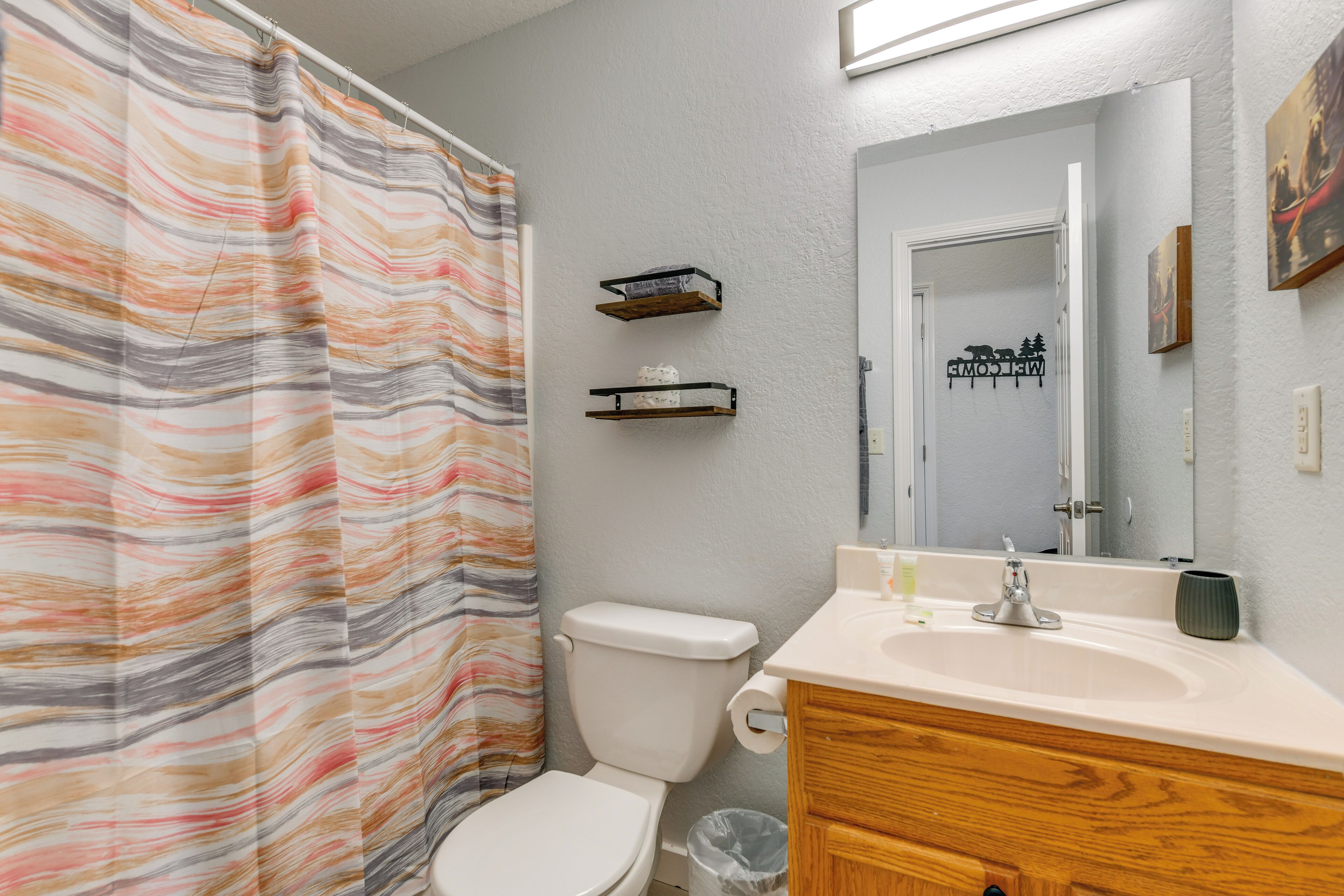Un bagno con tenda da doccia a righe, un water, un mobile bagno in legno, un lavandino e uno specchio.