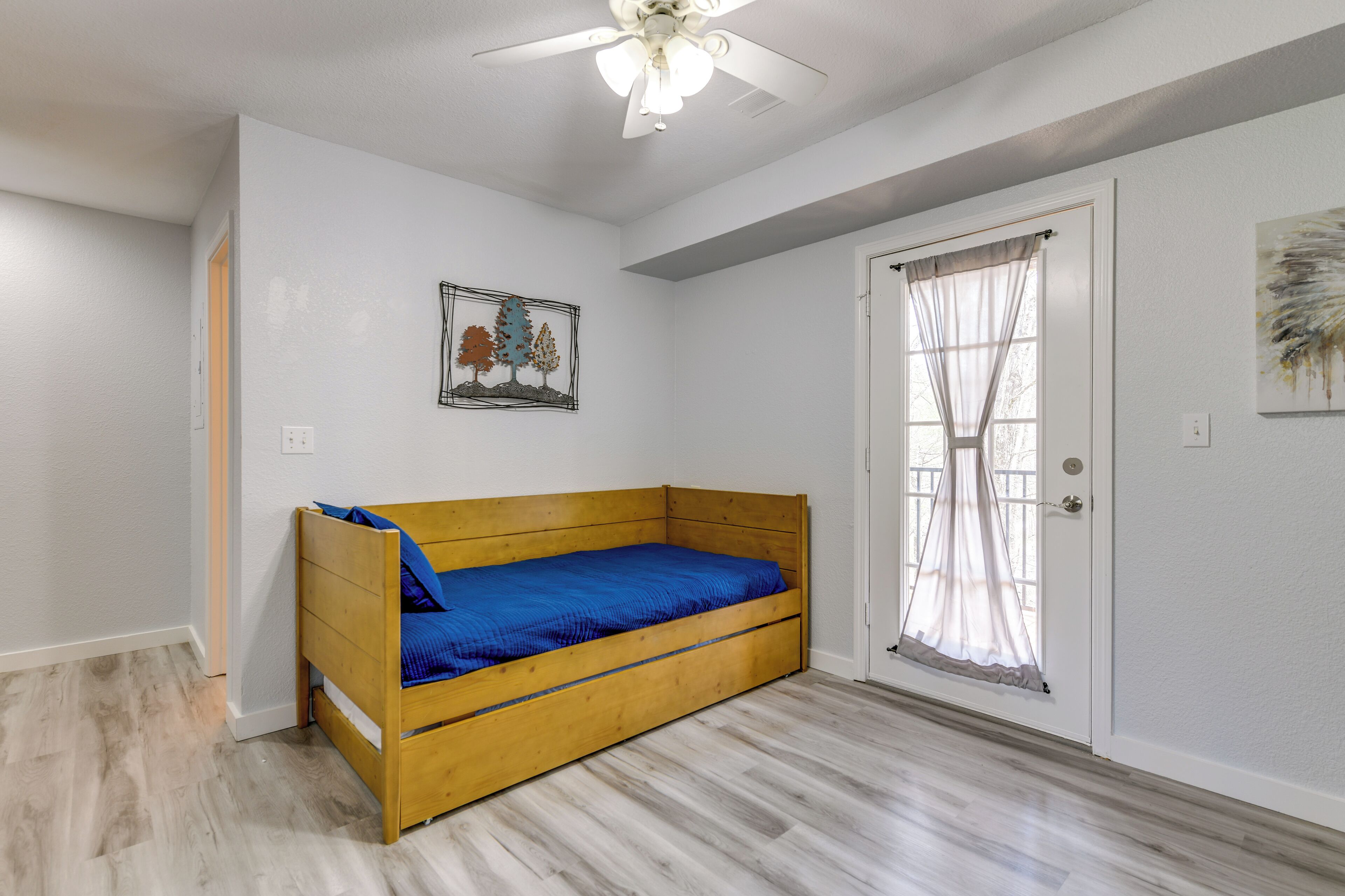A room with a wooden bed, a ceiling fan, a door with a window, and a wall-mounted picture.