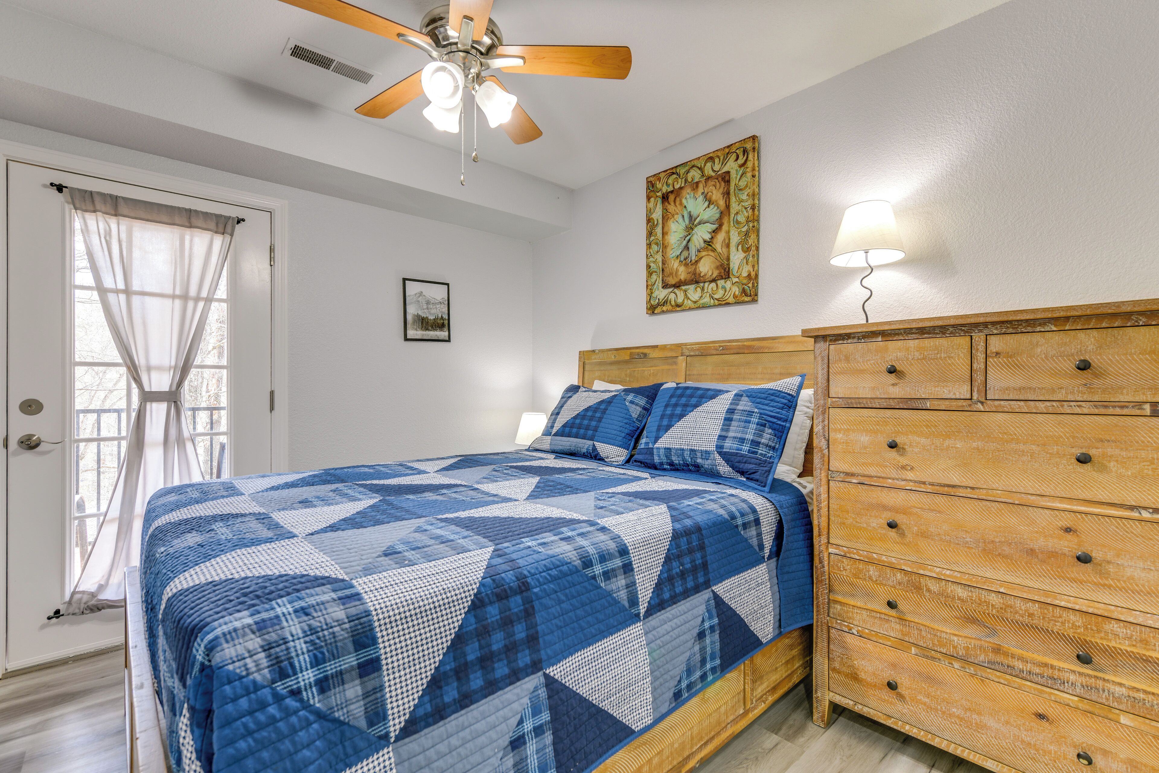 A bedroom with a bed, wooden dresser, ceiling fan, and a painting on the wall.