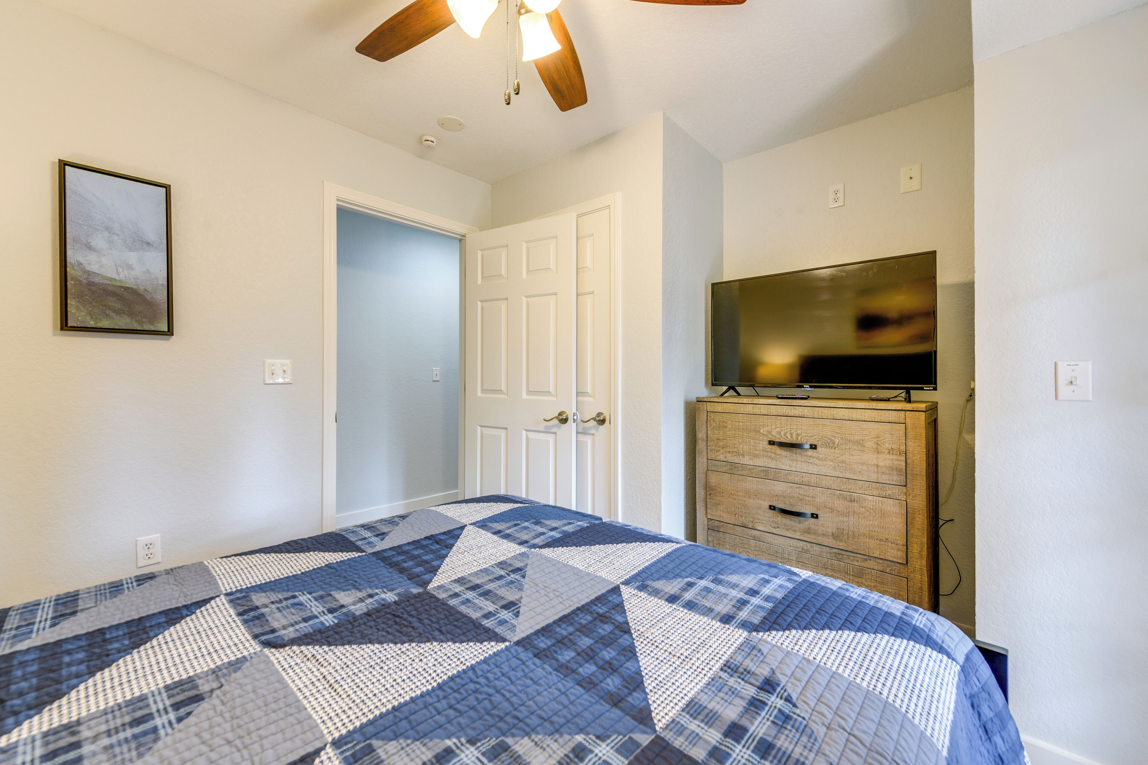 A bedroom with a bed, a wooden dresser, a television, and a ceiling fan.