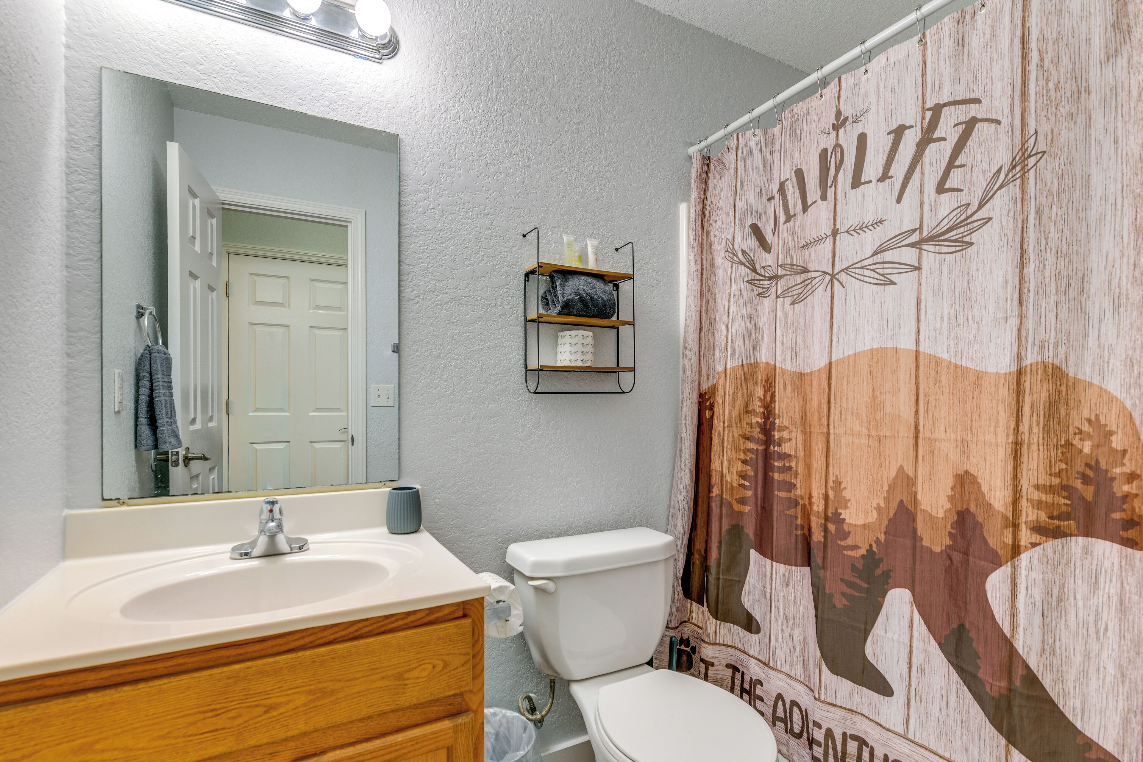 A bathroom with a white sink, wooden vanity, a toilet, a shower curtain with a wildlife design, and a mirror above the sink.