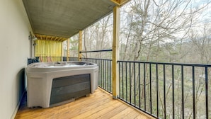 Un terrazzo in legno con vasca idromassaggio, ringhiera e vista sugli alberi.