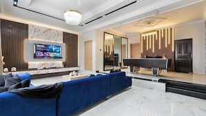 Una sala de estar moderna con un sofá azul, un televisor de pantalla plana, una mesa de billar y un piso de mármol.