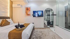 Una habitación de hotel moderna con cama, televisión y zona de ducha con vidrio.