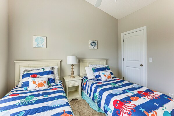 Une chambre avec deux lits, chacun agrémenté d’une parure assortie à rayures bleues et blanches, ornée de motifs représentant des créatures marines. On y trouve deux tables de chevet avec des lampes, et les murs sont peints dans une couleur beige clair.