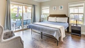 A bedroom with a bed, bedside tables, a chair, and a view through a sliding glass door to an outdoor area. - 3 Mi to Pier Village: Dog-friendly St Simons Home! (St. Simons Island)