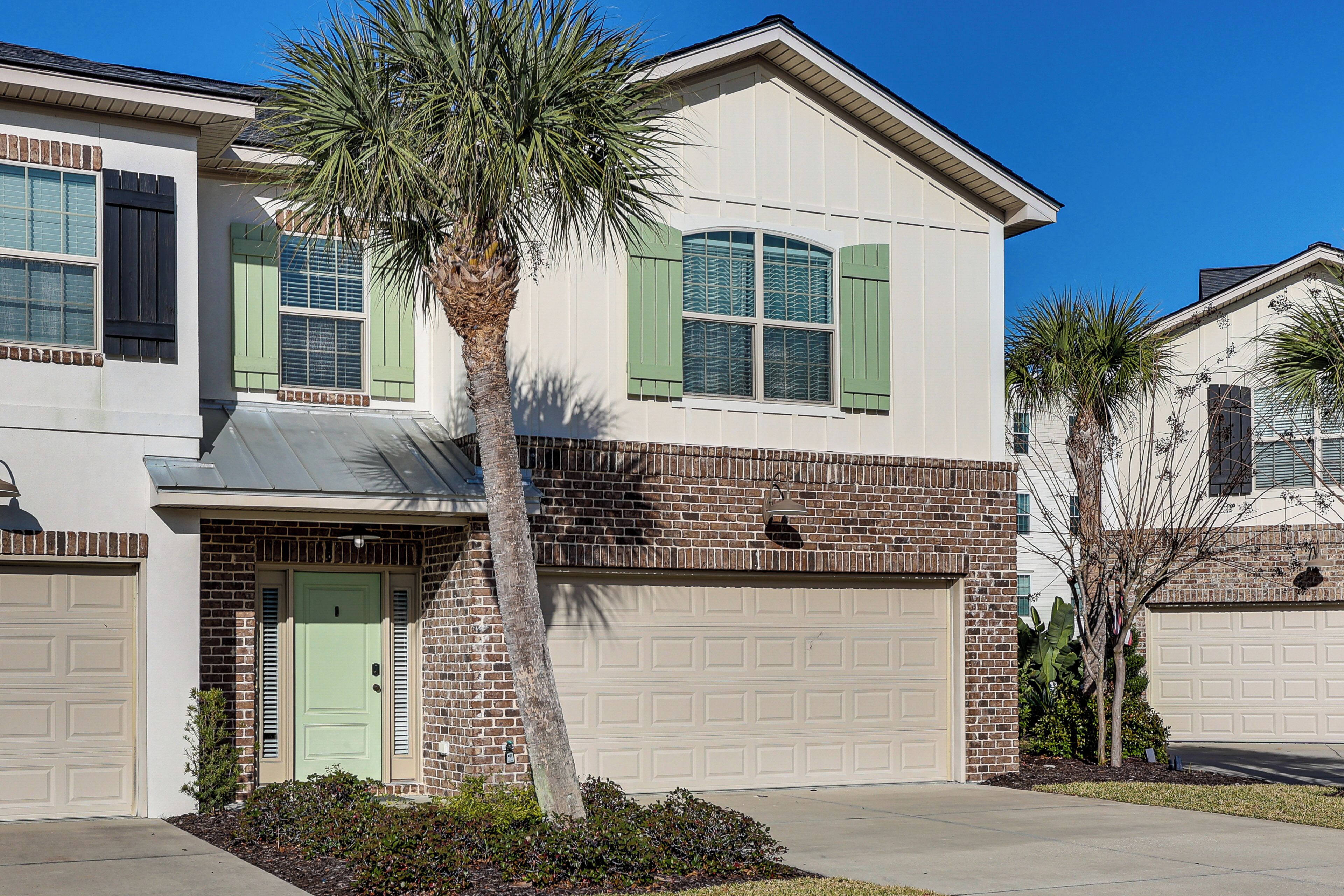 A two-story house with a garage, a green door, and a palm tree in the front yard.