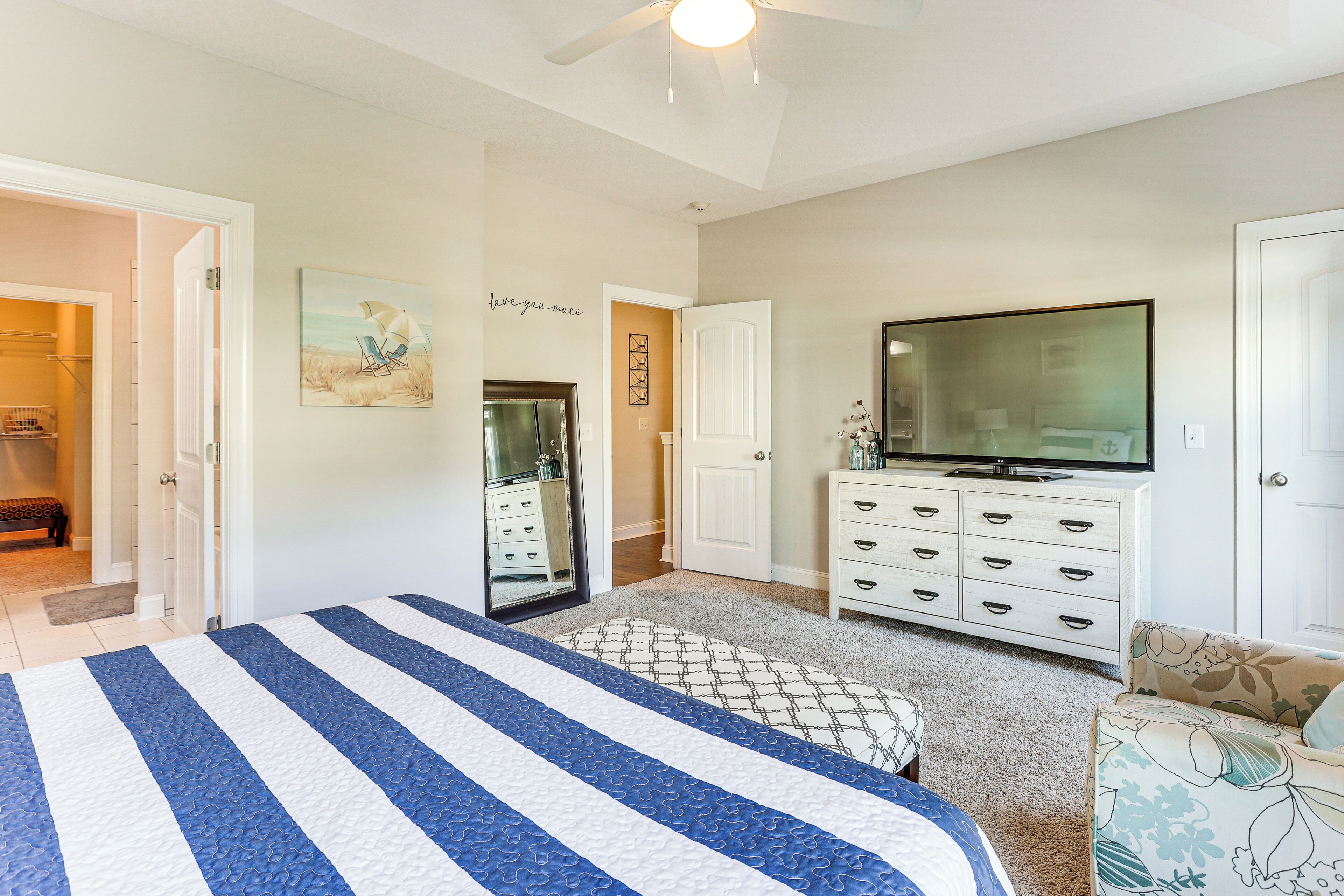 A bedroom with a bed, a dresser, a television, and a door leading to another room.