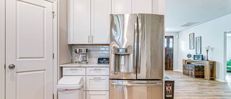 A modern kitchen with white cabinets, stainless steel appliances, and a wooden floor.