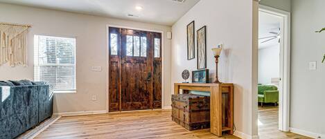 A spacious room with hardwood flooring, a large wooden door, a blue sofa, and a wooden table with a lamp.