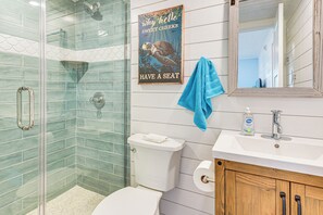 A bathroom with a glass shower enclosure, a white toilet, a sink with a soap dispenser, and a wooden cabinet. - Near Beaches: Waterfront Gem in Anna Maria Island! (Holmes Beach)
