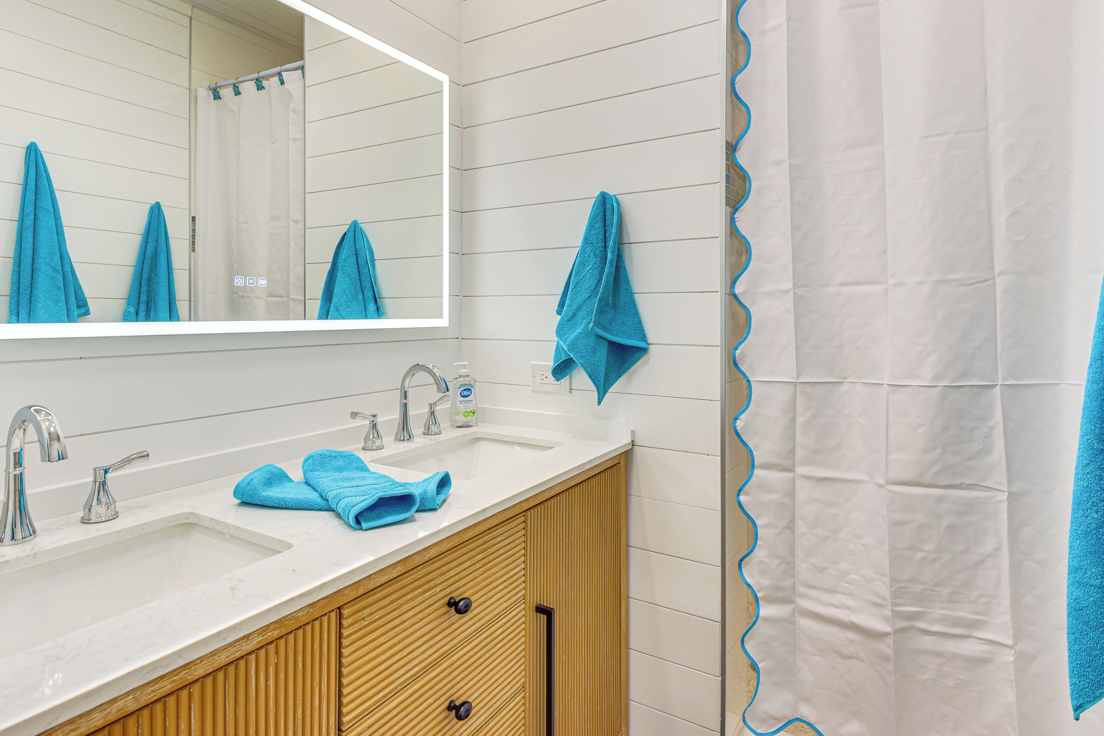 A bathroom with a white sink, wooden vanity, and a mirror.