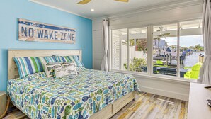 A bedroom with a bed, a ceiling fan, a window with a view of a marina, and a sign that reads "NO WAKE ZONE". - Near Beaches: Waterfront Gem in Anna Maria Island! (Holmes Beach)