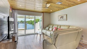 A modern living room with a leather sofa, a flat-screen TV, and a sliding glass door leading to a pool area. - Near Beaches: Waterfront Gem in Anna Maria Island! (Holmes Beach)