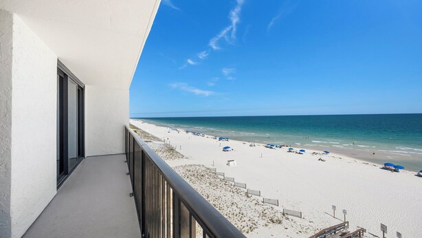 Un balcon avec vue sur une plage, un ciel dégagé et une rive sablonneuse.