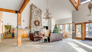 A spacious lobby with a stone wall, wooden beams, a fireplace, a Christmas tree, and a reception desk. - Walk to Ski Lift & Hot Tubs! Mtn-view Keystone Gem (Keystone)