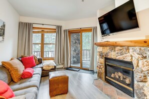 Un salón acogedor con chimenea, un ventanal grande y un televisor de pantalla plana montado en la pared.