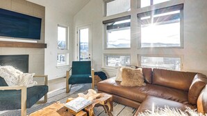 Ett rymligt vardagsrum med en öppen spis, en soffa i läder och stora fönster med utsikt över bergen.