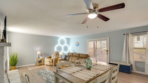 Un salón amplio con comedor, ventilador de techo y un gran ventanal con cortinas.