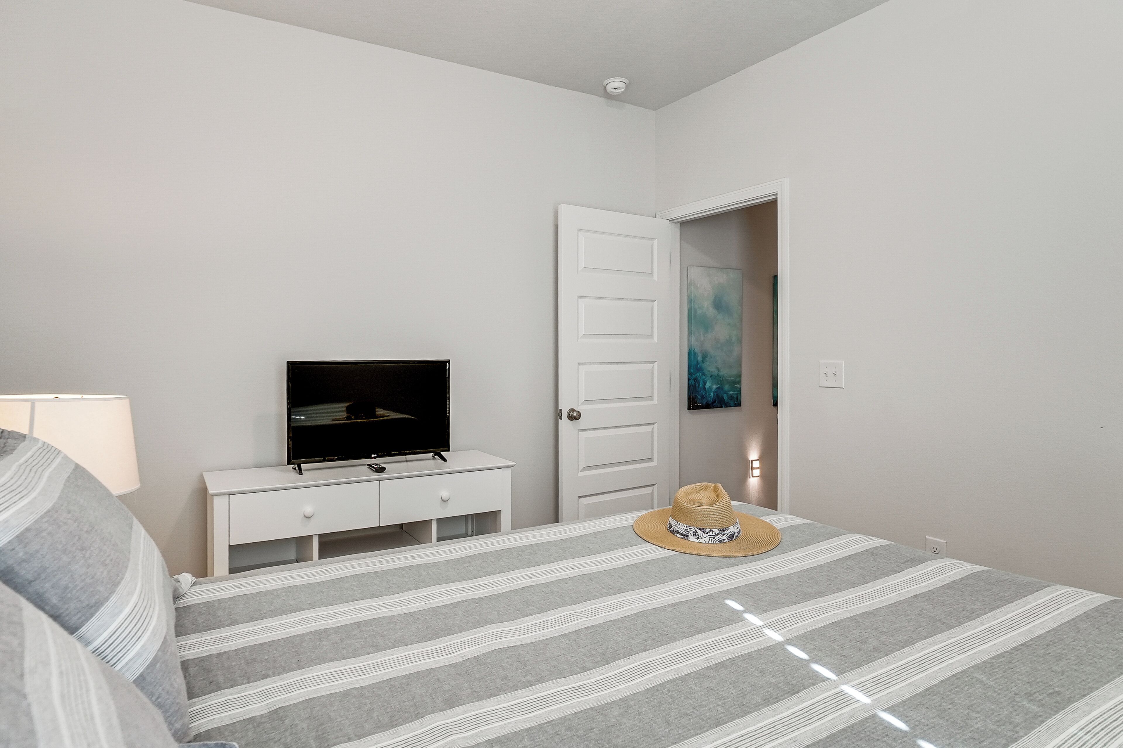 A bedroom with a bed, a TV on a white dresser, a door, and a hat on the bed.