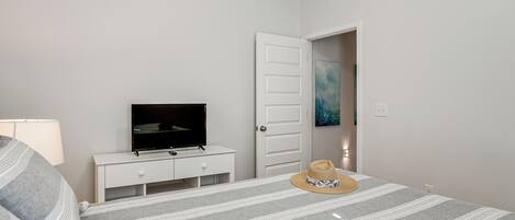 A bedroom with a bed, a TV on a white dresser, a door, and a hat on the bed.
